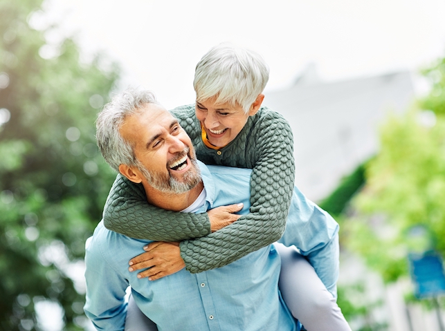 A senior couple overlayed in blue looks at each other smiling against a pink background.